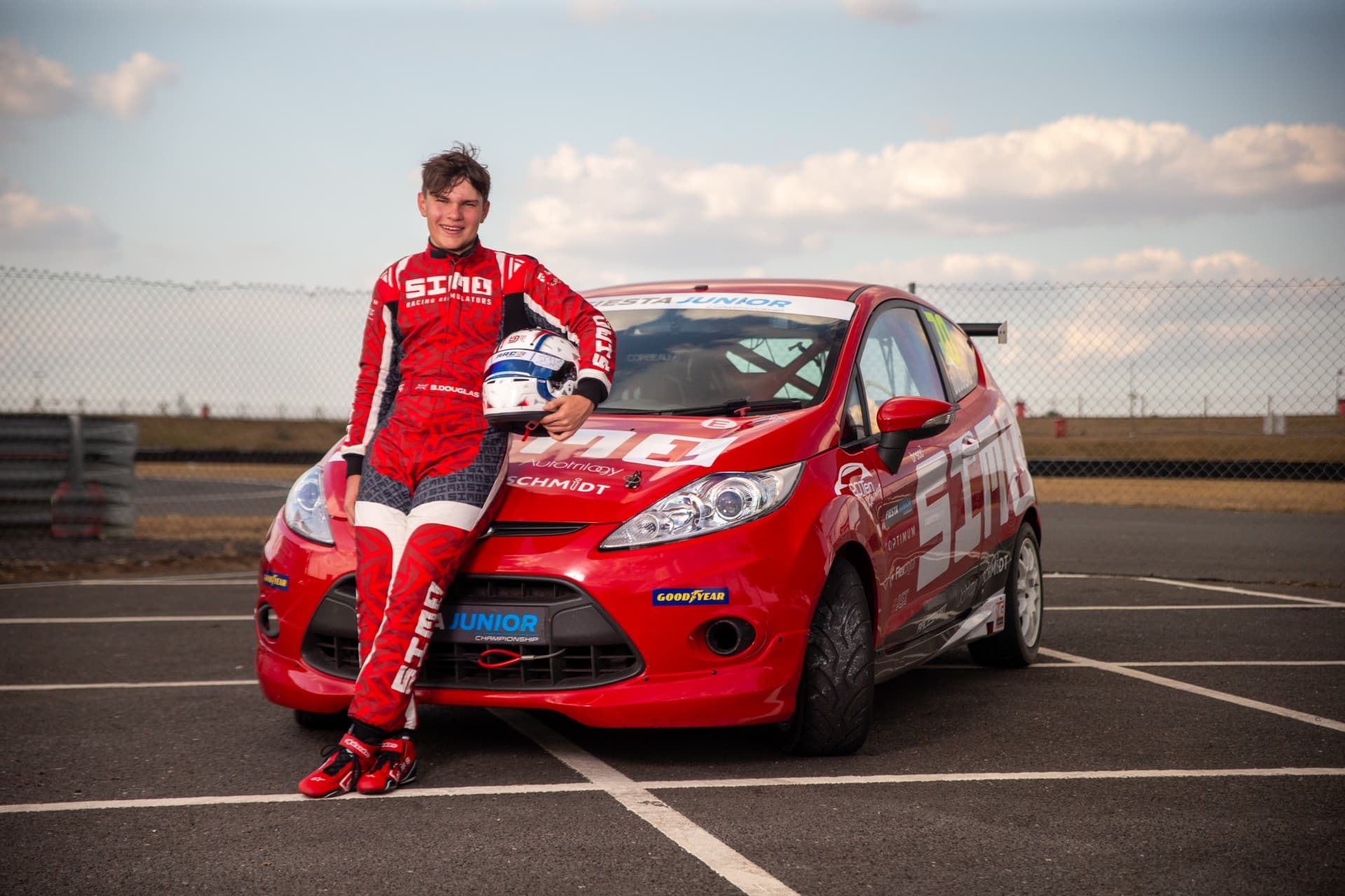 Benjy Douglas in his bright red Racecaft leaning against his Fiesta Junior race car