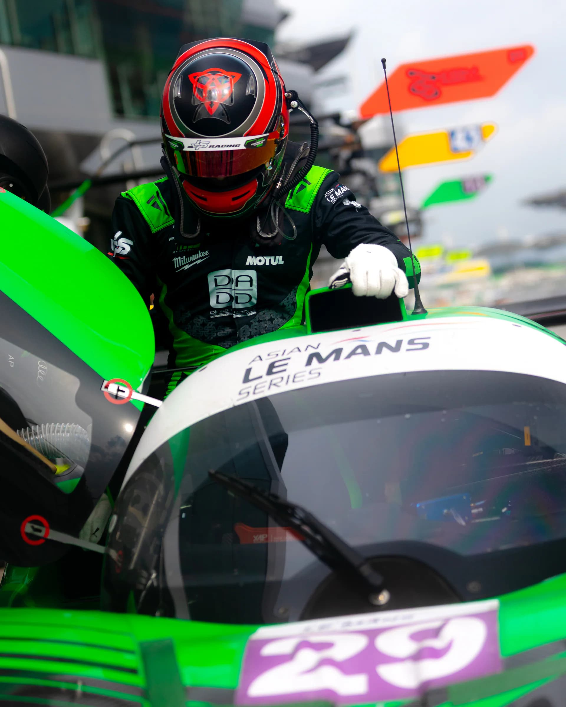 Helmeted driver in a black and green Torq Superlight race suit climbing into a prototype race car.