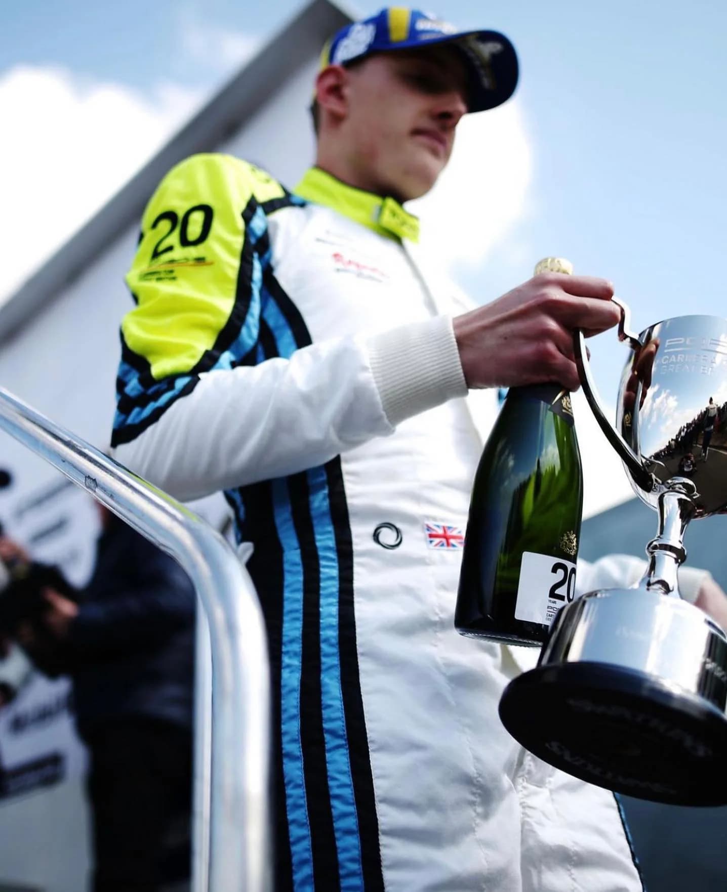 Driver in a white, fluorescent yellow and blue Torq Superlight race suit celebrating with champagne and a trophy.